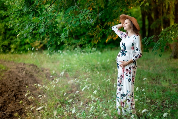 Uma mulher grávida com um vestido caminha na natureza na floresta no verão