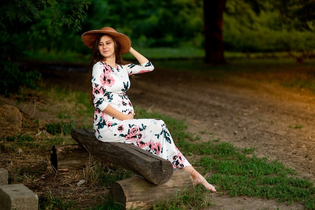 Uma mulher grávida com um vestido caminha na natureza na floresta no verão