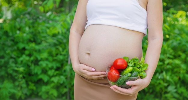 Uma mulher grávida com vegetais nas mãos. Foco seletivo. Comida.