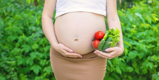 Uma mulher grávida com vegetais nas mãos. Foco seletivo. Comida.