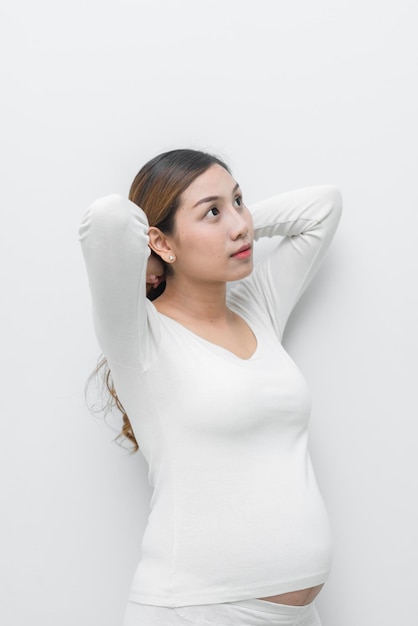 Uma mulher grávida de vestido branco faz pose para tirar uma foto no fundo branco