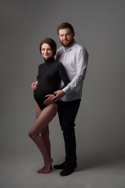 Uma mulher grávida e seu marido estão se abraçando em um fundo cinza. casal esperando um bebê.