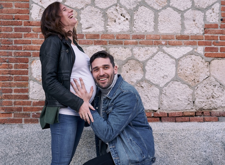 Foto uma mulher grávida em frente a um prédio de tijolos. homem abraça sua barriga. casal.