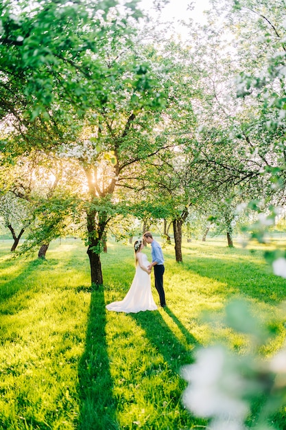 Uma mulher grávida em um vestido branco e uma coroa de flores na cabeça, ficar com o marido no jardim florescendo ao sol.