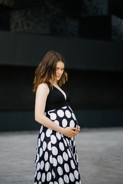 Uma mulher grávida em um vestido preto e branco segura as mãos na barriga dela