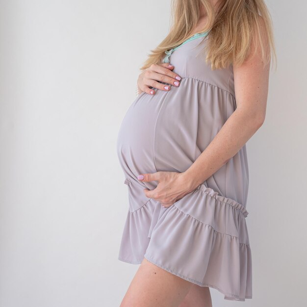 uma mulher grávida em uma camisola lilás pálida fica em um fundo branco