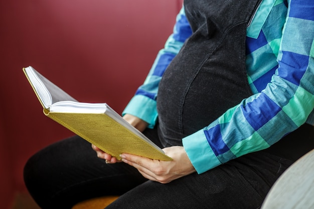 Uma mulher grávida está sentado com um livro nas mãos dela.