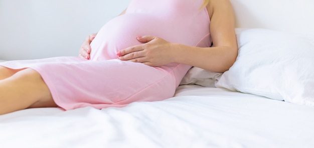 Uma mulher grávida na cama abraça o estômago