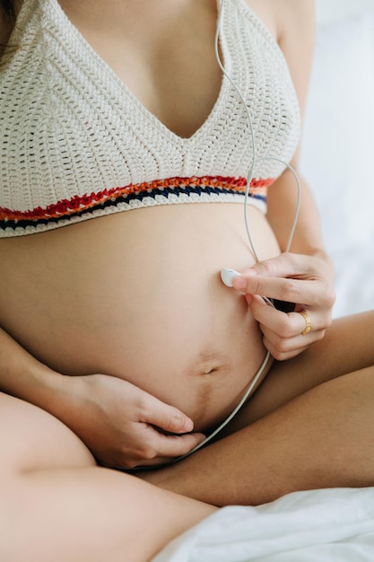 Uma mulher grávida se senta na cama tocando música para seu filho