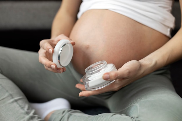 Uma mulher grávida segura um pote de creme na mão