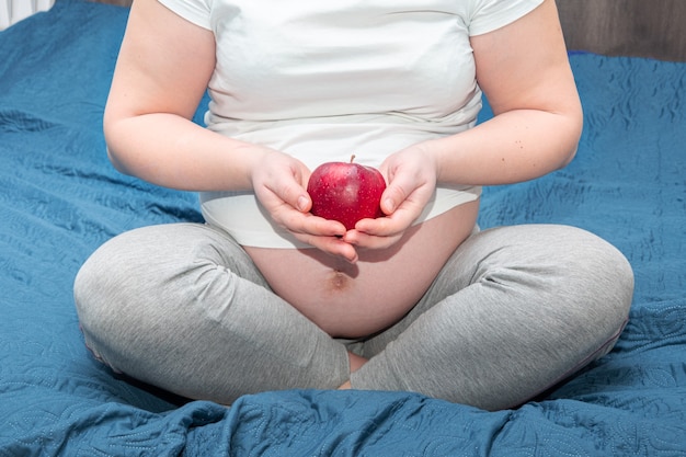 Uma mulher grávida segura uma maçã vermelha nas mãos. mulher grávida saudável comendo uma maçã rica em vitamina.