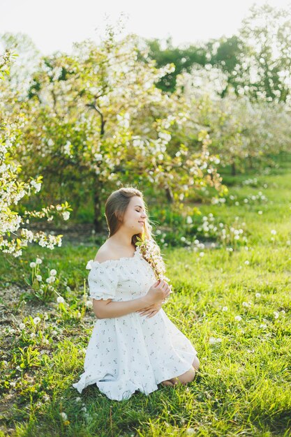 Uma mulher grávida sorridente com um vestido branco claro caminha em um jardim de primavera verde Uma mulher está esperando um filho Uma mulher grávida feliz na natureza