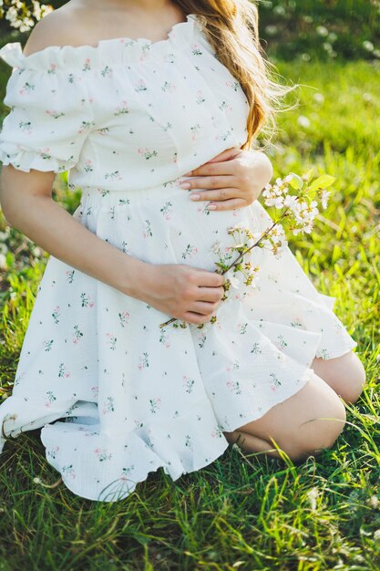 Uma mulher grávida sorridente em um vestido branco leve caminha em um jardim verde primavera Uma mulher está esperando um filho Mulher grávida feliz na natureza