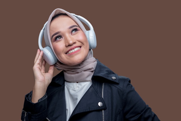 Uma mulher hijab estava ouvindo música usando fones de ouvido sem fio com uma expressão sorridente enquanto olhava para cima