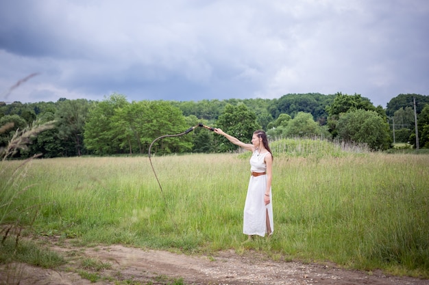 Uma mulher húngara em pé no campo com um vestido de linho e um chicote