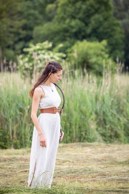 Uma mulher húngara em um vestido de linho com um arco está de pé no campo