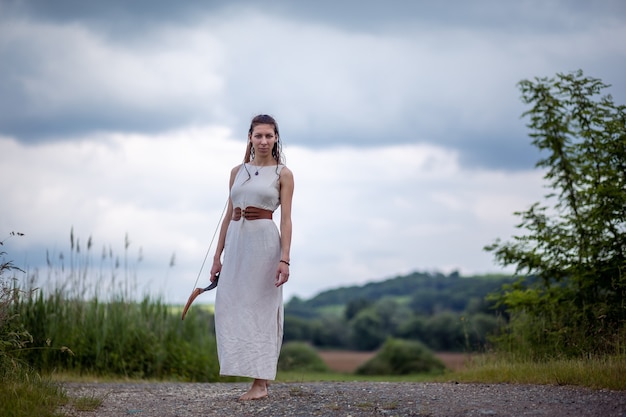 Uma mulher húngara em um vestido de linho com um laço está parada na estrada