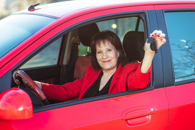 Uma mulher idosa foi presenteada com um carro vermelho. a vovó segura as chaves e sorri