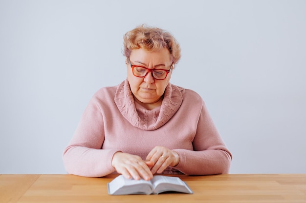 Uma mulher idosa sentada em sua casa profundamente absorta em seu livro enquanto usava seus óculos e desfrutava