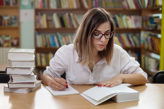 Uma mulher inteligente com óculos estudando na biblioteca com livros