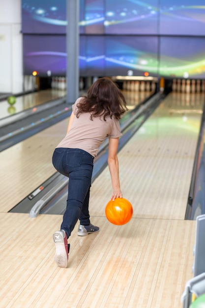 Uma mulher joga uma bola em uma pista de boliche. Caminhos com bolas e pinos para boliche.