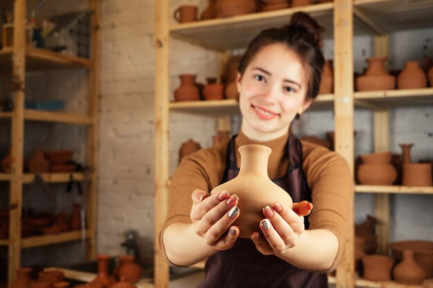 Uma mulher jovem e alegre segurando um vaso de barro. o oleiro trabalha em uma oficina de olaria com barro. o conceito de maestria e criatividade em cerâmica.