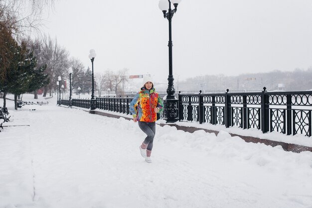 Uma mulher jovem e bonita está correndo em um dia gelado e com neve. Esportes, estilo de vida saudável