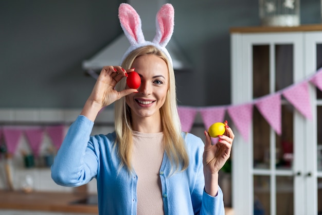Uma mulher jovem e feliz nos ouvidos do coelho colocou um ovo de Páscoa pintado no olho