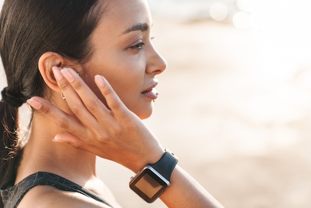 uma mulher jovem muito concentrada forte fitness ao ar livre na praia na manhã ouvindo música com fones de ouvido.