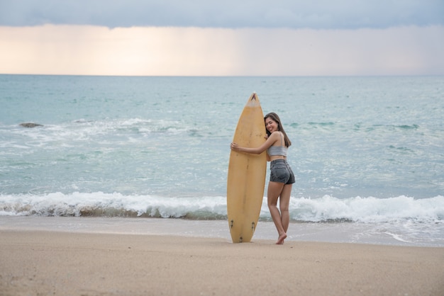 Uma mulher jovem sexy asiática andando na praia com prancha de surf em Phuket Tailândia