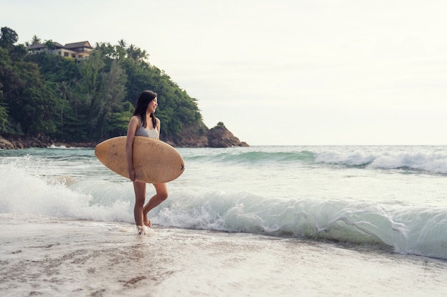 Uma mulher jovem sexy asiática andando na praia com prancha de surf em Phuket Tailândia