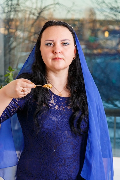 Uma mulher judaica com a cabeça coberta de uma capa azul na mesa do seder da páscoa come haroset
