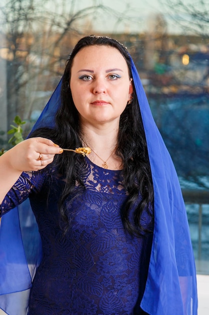 Foto uma mulher judaica com a cabeça coberta de uma capa azul na mesa do seder da páscoa come haroset