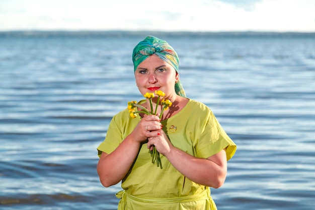 Uma mulher judia em um vestido verde e lenço no lago com nenúfares nas mãos em um dia ensolarado