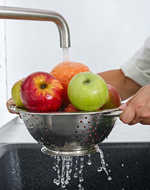 Uma mulher lava frutas com água corrente na cozinha.