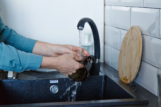 Uma mulher lava pratos. lavando o copo na pia preta