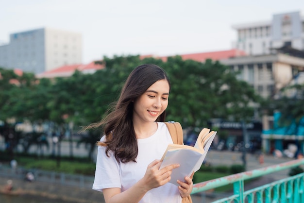Uma mulher linda sorridente lendo um livro enquanto está de pé ao ar livre
