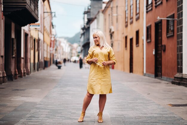 Uma mulher loira com um vestido de verão amarelo fica na rua da cidade velha de La Laguna, na ilha de Tenerife. Espanha, Ilhas Canárias.