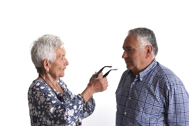 Uma mulher mais velha colocando óculos para um homem mais velho em fundo branco