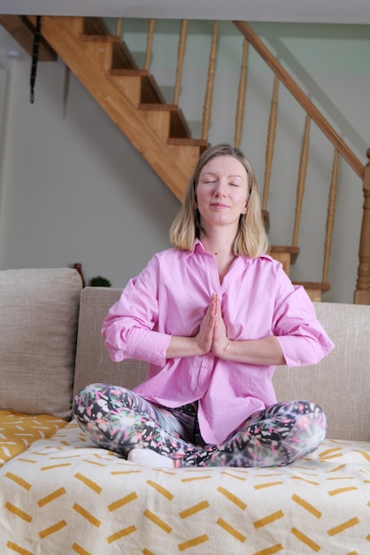 Uma mulher meditando em um sofá com um travesseiro listrado de amarelo e branco atrás dela.