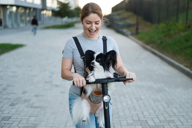 Foto uma mulher monta uma scooter elétrica com um cachorro em uma mochila pappilion spaniel continental em um esboço