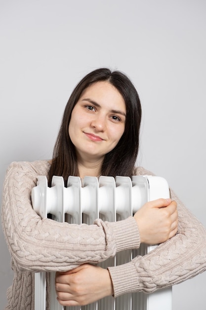 Uma mulher morena abraça um aquecedor elétrico a óleo