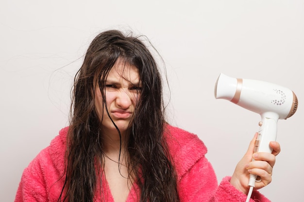 Uma mulher morena com cabelo emaranhado seca com um secador de cabelo cuidados com o cabelo cabelo ressecado