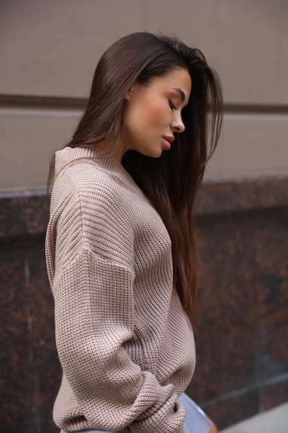 Uma mulher morena na rua com um suéter marrom e uma saia azul ao lado de um prédio bege estilo de vida cotidiano casual