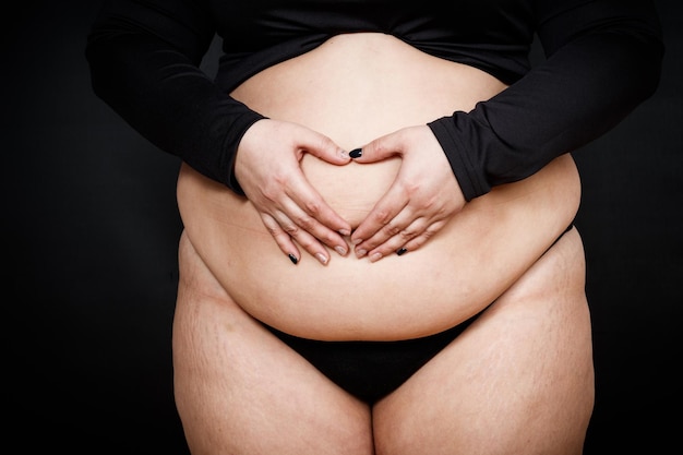 Uma mulher mostra um coração com as mãos em uma barriga gorda em um corpo de pessoa obesa de fundo preto positivi