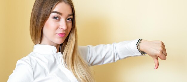 Uma mulher mostrando antipatia. jovem empresária linda vestindo uma camisa branca com o polegar para baixo isolado sobre um fundo amarelo.