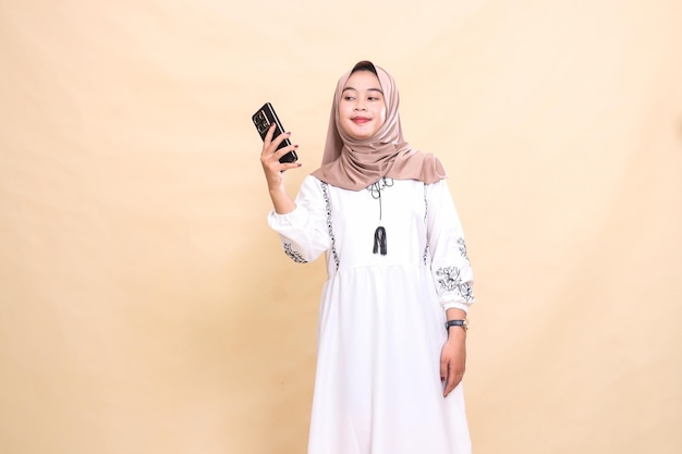 uma mulher muçulmana asiática adulta vestindo um hijab sorri à direita carregando um celular para criar conte