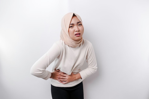Uma mulher muçulmana asiática está jejuando e com fome e tocando sua barriga enquanto olha de lado pensando no que comer