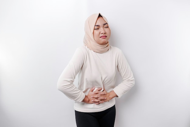 Uma mulher muçulmana asiática está jejuando e com fome e tocando sua barriga enquanto olha de lado pensando no que comer