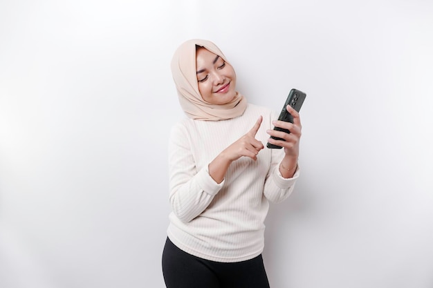 Uma mulher muçulmana asiática feliz usando um lenço na cabeça segurando seu telefone isolado por fundo branco